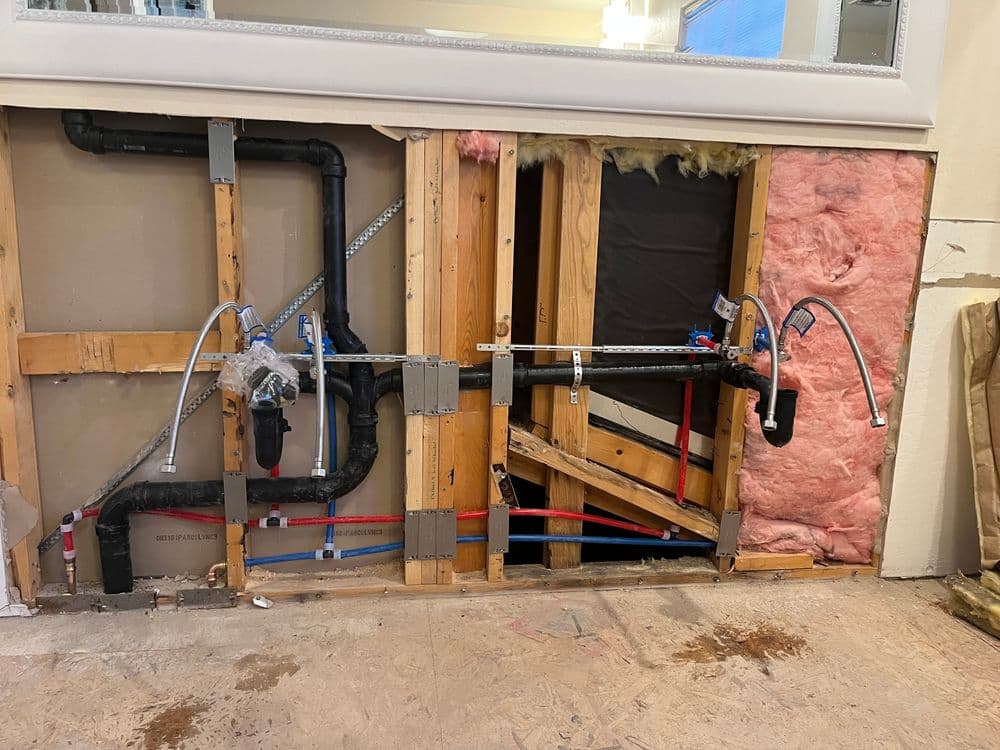 Exposed plumbing system in wall showing pipes, insulation, and framing for repair.